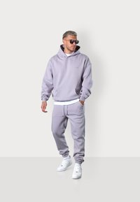 Hellblaue Hoodie und passende Jogginghosen aus weichem Stoff, mit einer vorderen Tasche und elastischen Bündchen, kombiniert mit weißen Turnschuhen.