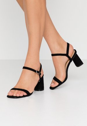 Sorte ruskind hælede sandaler med justerbare ankelremme, åben tå-design, tekstureret materiale og blok-hæle. Enkel og minimalistisk stil.