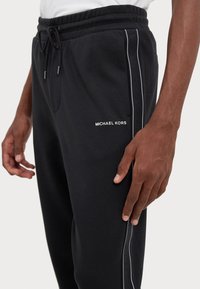 Black sweatpants with an elastic waistband, drawstring, and side stripes featuring "MICHAEL KORS" logo in white and subtle gray detailing.