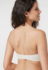Crème bandeau bh met een gladde stof, naadloos ontwerp en haaksluiting aan de achterkant. Verstelbare pasvorm met een zachte textuur.