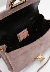 Vaaleanpunainen mokkahandbag, jossa on musta nahkasisustus, kultaiset yksityiskohdat ja brändilappu, jossa lukee "Aito italialainen nahka."