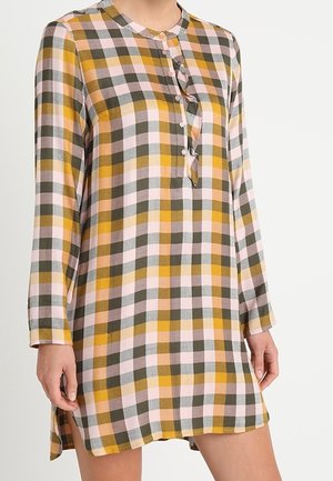 Langärmliges Kleid mit gelbem, olivgrünem und blassrosa Kariertem Muster, geknöpfter Blende und leichten Seitenschlitzen, getragen von einer stehenden Person.