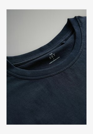 Marineblå bomulds t-shirt med rund halsudskæring, synlig syning og et mærke, der viser "THE SET, M, MADE IN BANGLADESH." Glat tekstur.