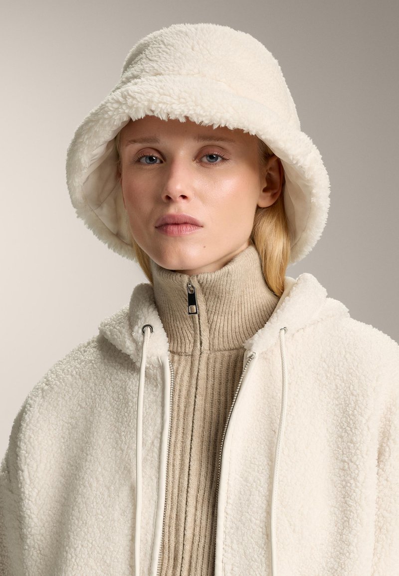 Kapa u obliku kante od kremaste flisa i bež upijajući visoki ovratnik, sa zatvaranjem na patentni zatvarač i špagom na kapuljači jakne.