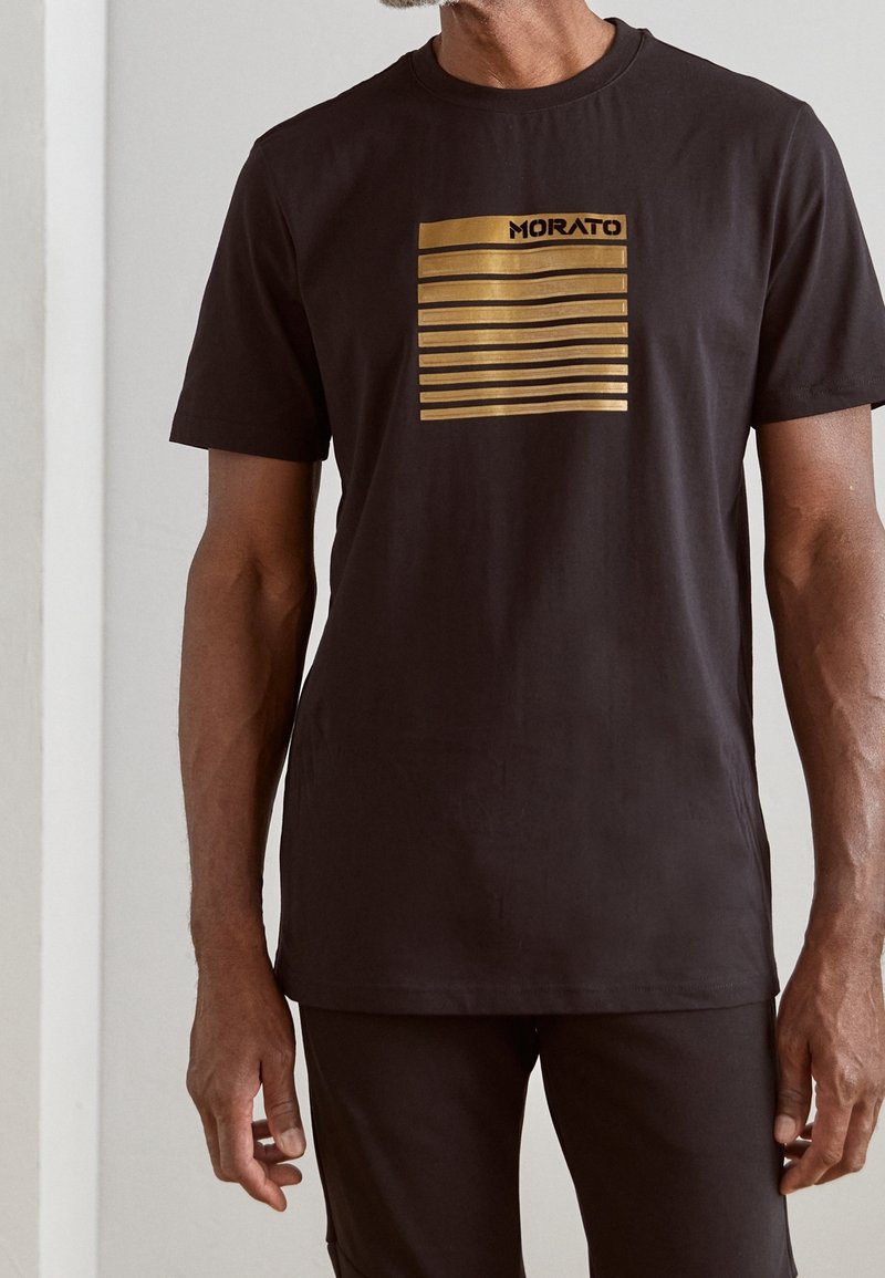 Black cotton t-shirt featuring a gold striped graphic design and "MORATO" text. Short sleeves and a crew neck. Smooth texture.