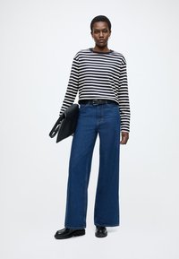 Bluză cu mâneci lungi, cu dungi albastre și albe, asortată cu blugi evazați din denim albastru. Curea neagră și geantă mică neagră completează ținuta.