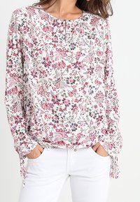 Blumenmuster-Bluse mit langen Ärmeln und weißem Hintergrund, mit rosa und grünen Mustern, einem runden Halsausschnitt und Knopfdetails an der Vorderseite.