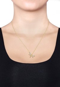 Gouden ketting met een zeester hanger, versierd met heldere edelstenen, geplaatst op een delicate ketting. G gedragen tegen een neutrale achtergrond.
