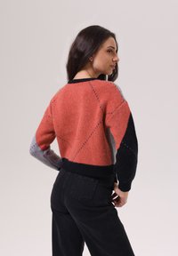 Pull en tricot avec un design en blocs de couleurs orange, gris et noir, doté d'un col rond et de poignets côtelés, porté avec un pantalon noir taille haute.