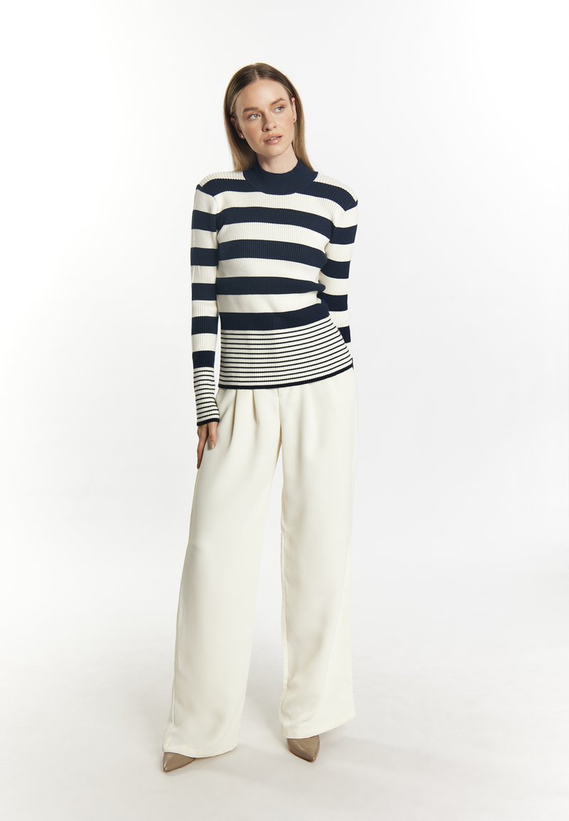 Gestreifter, navyblauer und weißer Strickpullover mit geripptem Textur und tailliertem Design. Kombiniert mit weit geschnittenen weißen Hosen und beigen Heels.