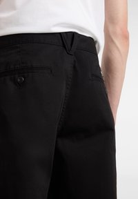Pantaloni neri in cotone, caratterizzati da una texture liscia, tasche standard e un dettaglio con un solo bottone sulla tasca posteriore.