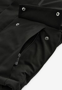 Schwarzer Outdoor-Jackenstoff mit Reißverschlusstasche, Druckknopfverschlüssen und matter Textur. Weiches Futter ist in der Tasche sichtbar.