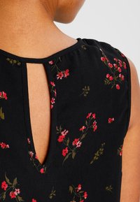 Svart blommig ärmlös topp med små rosa och gröna blommor. Har en nyckelhål-design på ryggen och ett mjukt, texturerat tyg.