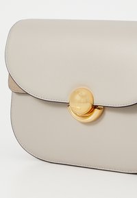 Borsa a tracolla in pelle grigio chiaro con patta arrotondata, accessori circolari in oro e cuciture a contrasto lungo i bordi. Texture liscia.