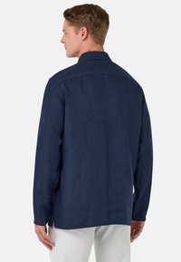 Donkerblauwe langemouwen shirt met een puntige kraag en rechte snit. De stof lijkt glad met een subtiele textuur en zijsplitten aan de zoom.