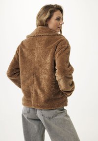 Bruine, fuzzy faux fur jas met een kraag, relaxte pasvorm en zichtbare naden, gecombineerd met lichtgrijze high-waisted jeans.