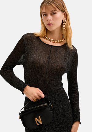 Schwarzes glitzerndes Kleid mit langen Ärmeln. Das Model hält eine kleine schwarze Handtasche mit einem goldenen Buchstaben "N" und einem strukturierten Kettenakzent.