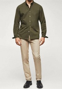 Camisa de botones color verde oliva con mangas largas, combinada con pantalones ajustados de color beige claro y botines negros. La tela parece suave.