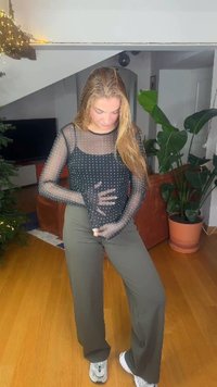 Čierny sieťovaný top s dlhými rukávmi s bielymi bodkami, v kombinácii so širokými olivovo zelenými nohavicami a bielymi teniskami na drevenej podlahe.