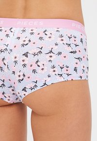 Bloemmotief ondergoed met een lichtblauwe basis, voorzien van roze en zwarte bloemen. De tailleband heeft "PIECES" in het roze gedrukt.