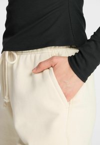 Schwarzes, geripptes Langarmoberteil kombiniert mit cremefarbenen Jogginghosen, die über einen elastischen Bund und Seitentaschen verfügen, und aus einem weichen, strukturierten Stoff bestehen.