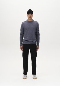 Szürke kötött pulóver bordás mandzsettával, fekete cargo nadrág zsebekkel és fehér sneakers világosbarna talppal. A modell egy fehér háttér előtt áll.