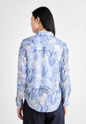 Blue floral blouse with long sleeves, featuring light and dark blue flower patterns, a collar, and buttoned cuffs. Back design includes a logo detail.