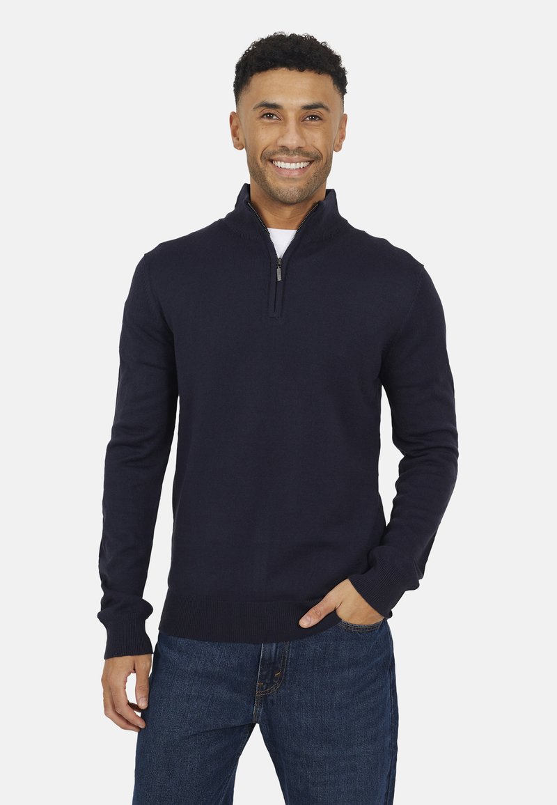 Maglione zip-up navy con maniche lunghe, polsini a coste e collo alto, abbinato a jeans blu. Materiale morbido con una consistenza liscia.