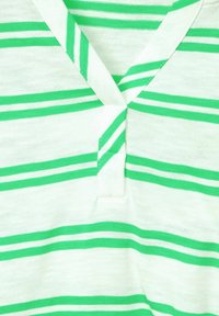 Zielono-biały materiał w paski z dekoltem w serek; posiada jeden mały guzik i miękką, lekką teksturę.