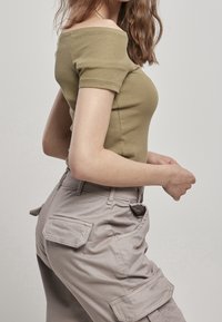 Top a spalle scoperte di un verde oliva a coste abbinato a pantaloni cargo beige chiaro con tasche laterali e tessuto testurizzato.