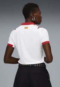 Witte polo met rode kraag en manchetten, met subtiele graphics op de achterkant. Ontworpen met korte mouwen en een getailleerde snit.