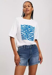 Biała bawełniana koszulka z niebieskim wzorem zebry, zestawiona z niebieskimi szortami z wysokim stanem, o klasycznym kroju i fakturze materiału.