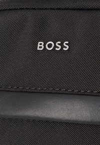 Zaino in tessuto nero con finitura texturizzata, dettagli in pelle nera opaca e logo "BOSS" in rilievo argentato sul fronte.