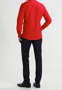 Rotes Langarmhemd mit schmaler Passform, ausgestattet mit einem Button-Down-Kragen und Manschettendetails, kombiniert mit schwarzen Anzughosen und Schuhen.