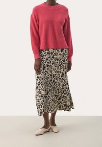 Różowy sweter dziany z okrągłym dekoltem, w połączeniu z midi spódnicą w panterkę w odcieniach beżu i czerni. Modelka nosi jasnobeżowe baleriny na odkrytej pięcie.