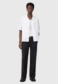Camisa blanca de manga corta con botones, superpuesta a una camiseta blanca de textura. Combinada con pantalones negros de corte holgado y zapatos negros.