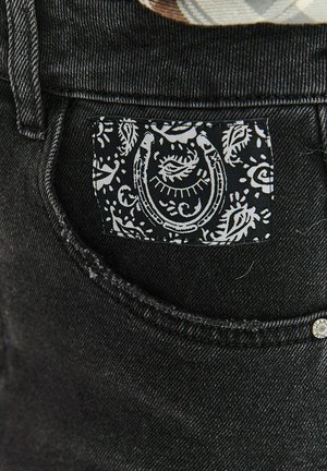 Czarny dżins o teksturowanej powierzchni; posiada biały etykietę z wzorem paisley i motywem podkowy na tylnej kieszeni.