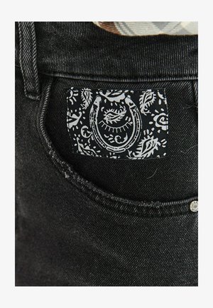Czarny dżins o teksturowanej powierzchni; posiada biały etykietę z wzorem paisley i motywem podkowy na tylnej kieszeni.