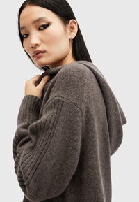 Felpa con cappuccio lavorata a maglia in grigio scuro, con maniche a coste e una vestibilità rilassata. Il tessuto appare morbido e caldo, con una leggera lucentezza.