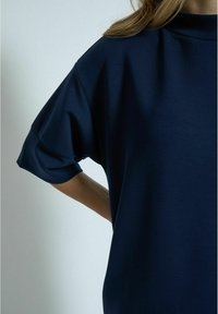 Tamno plavi oversized majica od glatkog materijala s kratkim rukavima i okruglim izrezom. Ima opušteni kroj i minimalni dizajn.