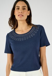 Top blu navy a maniche corte con scollatura rotonda, caratterizzato da un design di perline attorno al colletto e una texture liscia.