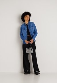 Camisa de ganga, azul, com dois bolsos no peito; top cropped preto, calças largas; bolsa mini prateada; sapatos pretos; cabelo texturizado; fundo neutro.