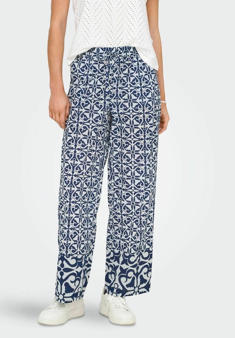 Navy plave šire hlače s uzorkom i pojasom na vezanje, s ponavljajućim cvjetnim dizajnom u bijeloj boji, u kombinaciji s bijelim tenisicama.