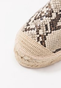 Chaussure espadrille avec une semelle en jute tissée beige texturée, un dessus à motif serpent en crème et noir, avec des coutures le long du bord.