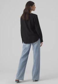 Maglietta nera a maniche lunghe con orlo arrotondato, abbinata a jeans larghi azzurri. L'outfit presenta una vestibilità comoda e un design minimal.