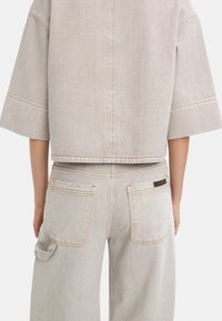 Jasnoszara top z denimu z krótkim rękawem, prostym krojem i kontrastowym przeszyciem. W zestawie z jasnoszarymi, zwolnionymi dżinsami o wysokim stanie.