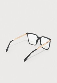 Čierne obdĺžnikové okuliare so zlatými kovovými stranami. Rám má matný povrch a priehľadné šošovky. Na ramene je viditeľné logo značky.