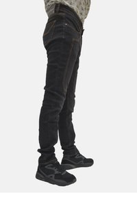 Jeans slim neri in denim con cuciture arancioni, dotati di tasche anteriori e posteriori. Abbinati a sneaker sportive nere per un contrasto.