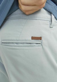 Jasnoniebieskie spodnie z tylną kieszenią o skośnym kroju i brązową skórzaną metką z napisem "JACK&JONES". Gładka tekstura materiału.