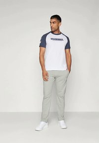 Λευκό μπλουζάκι με μπλε μανίκια, με το λογότυπο "HUMMEL". Γκρι φόρμες και λευκά αθλητικά παπούτσια ολοκληρώνουν την εμφάνιση. Απλός σχεδιασμός, casual εφαρμογή.